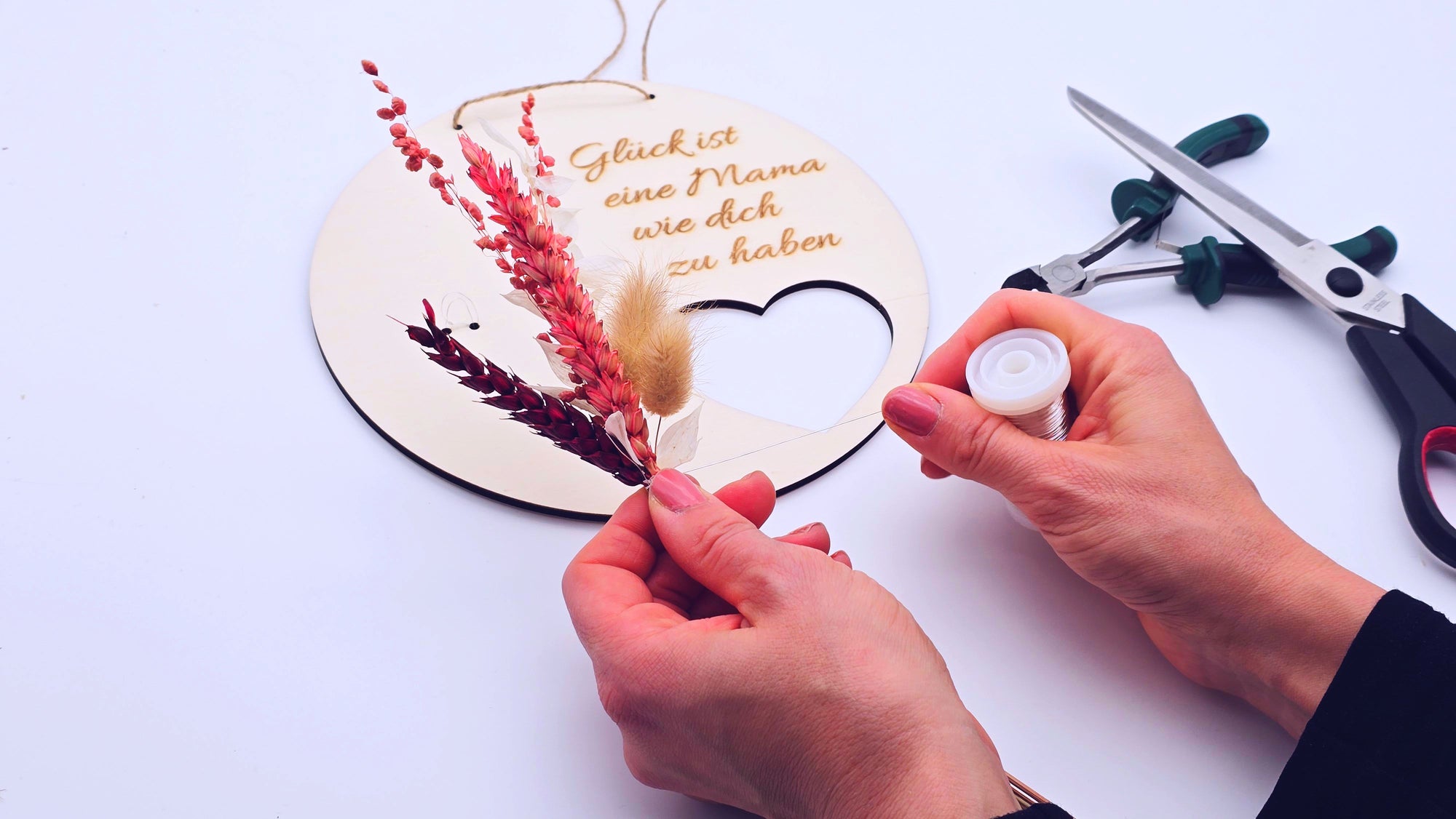 Auf diesem Bild wird ein kleines Sträußchen aus Trockenblumen gebunden, um es anschließend auf einem Holzschild zu befestigen.