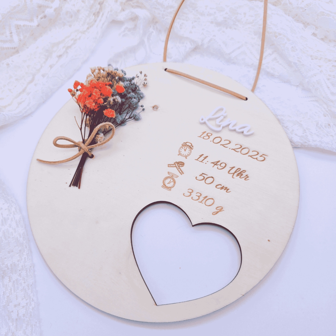 Personalisiertes Geburtsgeschenk mit Namensschriftzug aus weißem Acryl und Trockenblumen, auf runder Holzscheibe arrangiert