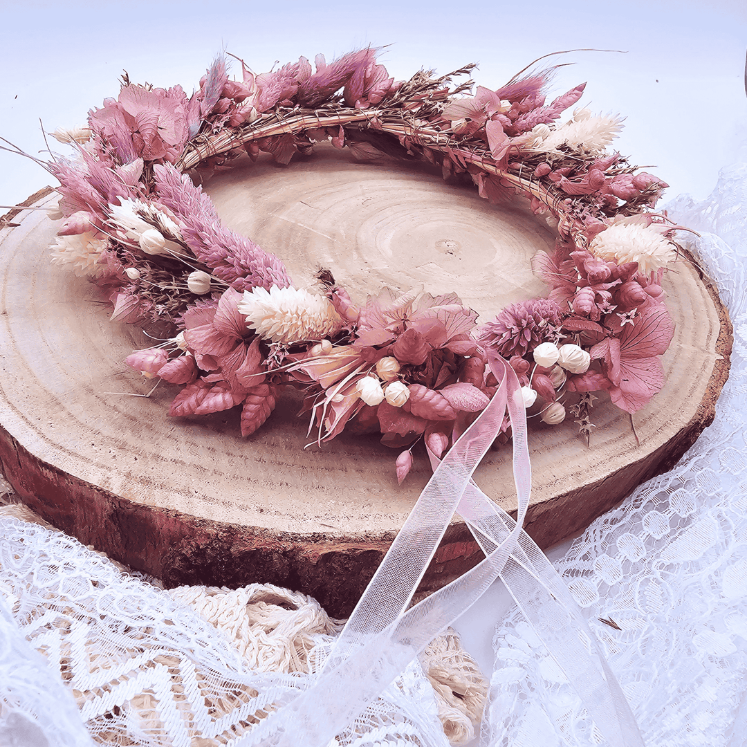 Handgefertigter Blumenkranz aus rosa und lila Trockenblumen mit zartem Band – dekorativ auf Holzscheibe inszeniert, ideal für Hochzeit, Boho-Look oder als Haarkranz.